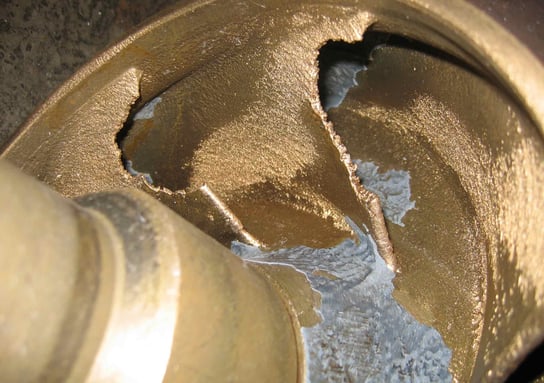 A pump impeller has been pitted and broken due to cavitation damage. Pieces of the impeller blades are missing.